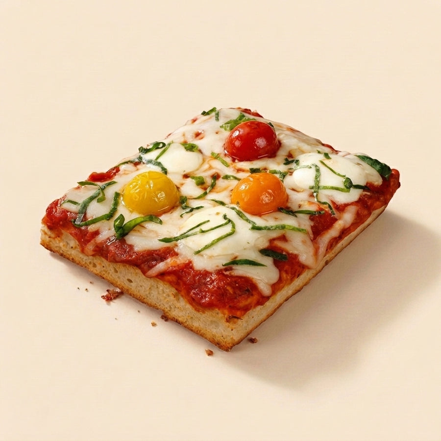 A square slice of artisanal pizza with tomato sauce, melted white cheese, green herb garnish, and whole cherry tomatoes on a light beige background.
